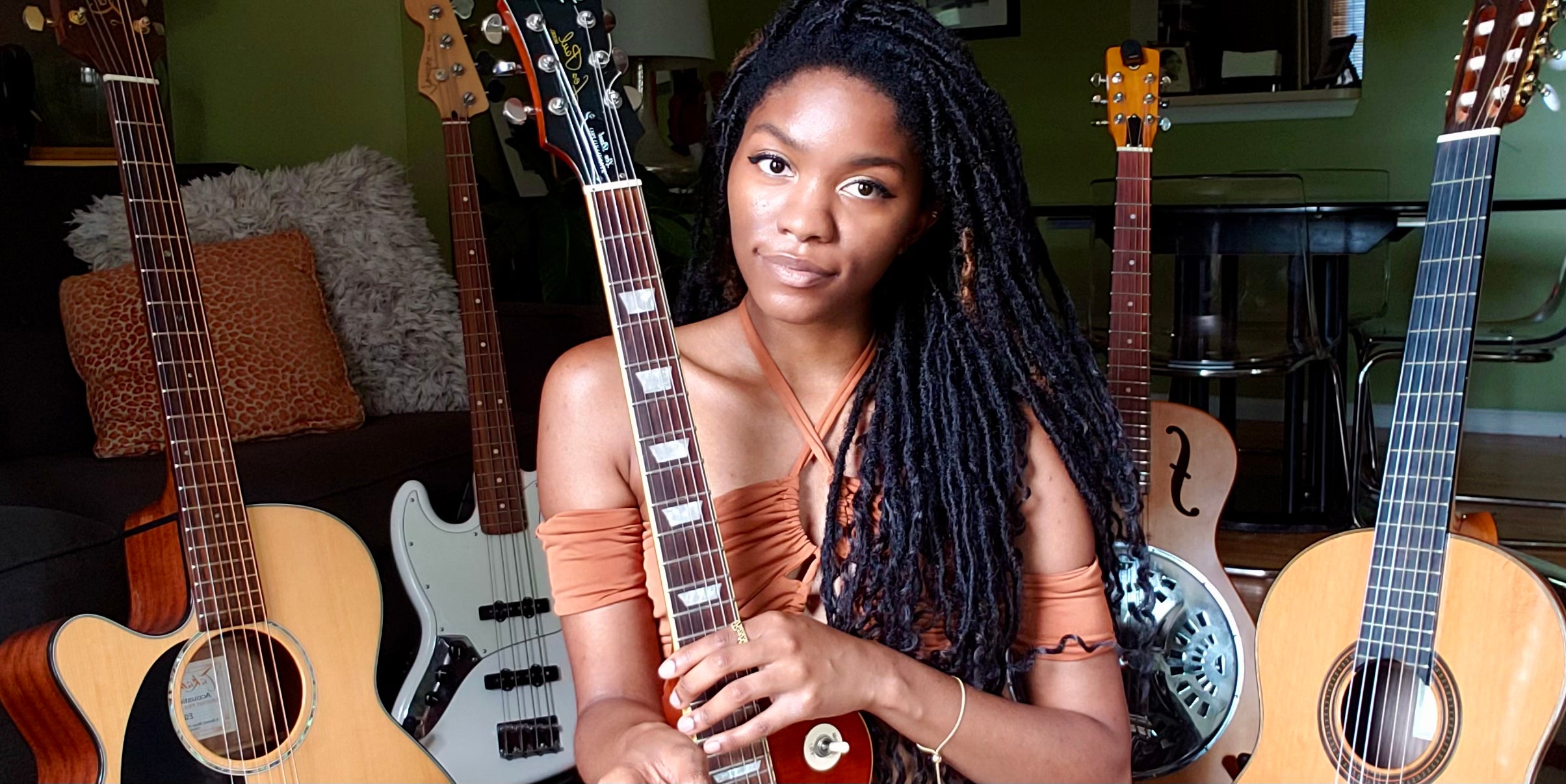 Baltimore, Maryland musician Evan Nicole Bell poses with her Epihone Les Paul electric guitar. Behind her are 4 of her other instruments: a Takamine acoustic guitar, Fender jazz bass, Epiphone Dobro Hound Dog, and a classical guitar. 
